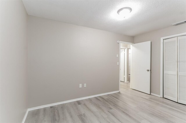 unfurnished bedroom with a textured ceiling, light hardwood / wood-style flooring, and a closet