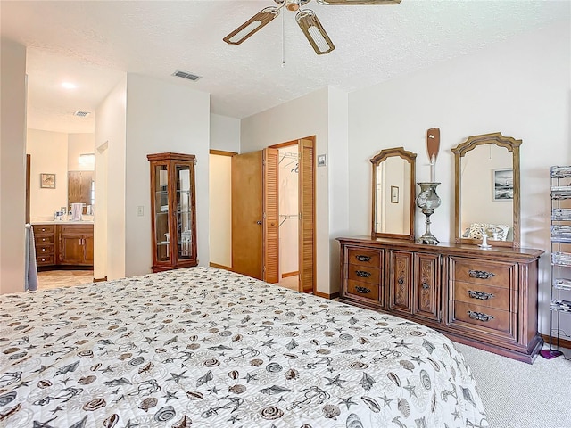 bedroom featuring connected bathroom, light carpet, a textured ceiling, a closet, and ceiling fan