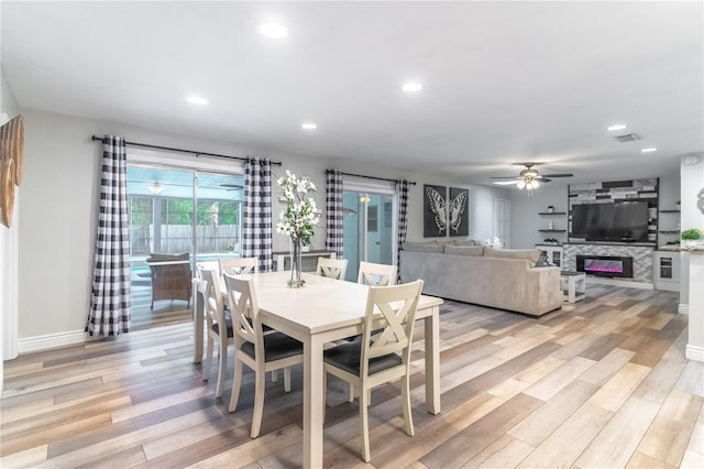 dining area with a fireplace, light wood-type flooring, and ceiling fan