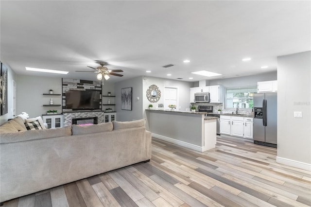 living room with a stone fireplace, sink, light wood-type flooring, and ceiling fan