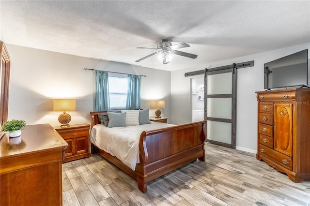 bedroom featuring light hardwood / wood-style flooring, a barn door, a textured ceiling, and ceiling fan