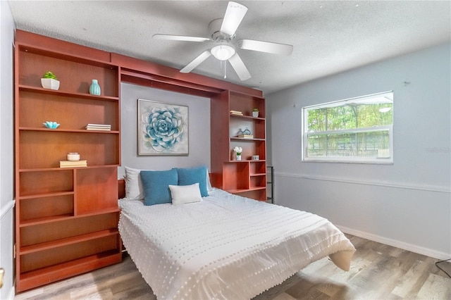 bedroom with a textured ceiling, wood-type flooring, and ceiling fan