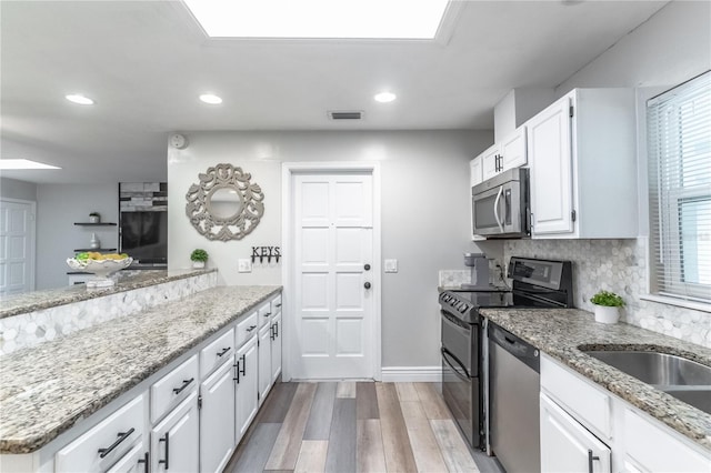 kitchen with white cabinetry, stainless steel appliances, light stone countertops, and light wood-type flooring