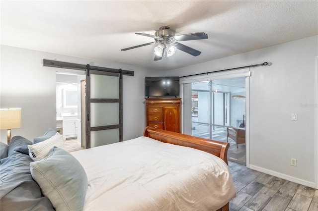 bedroom with connected bathroom, access to outside, a barn door, ceiling fan, and wood-type flooring