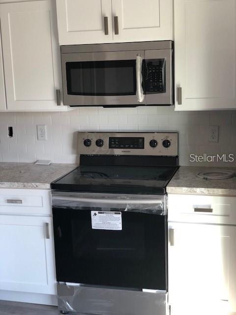 kitchen featuring stainless steel appliances, decorative backsplash, and white cabinetry