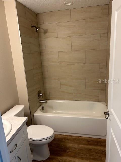 full bathroom with a textured ceiling, tiled shower / bath, hardwood / wood-style flooring, toilet, and vanity