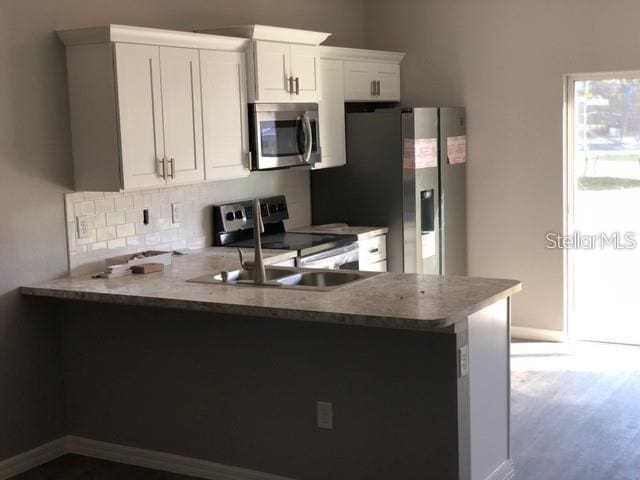 kitchen featuring appliances with stainless steel finishes, kitchen peninsula, decorative backsplash, sink, and white cabinetry