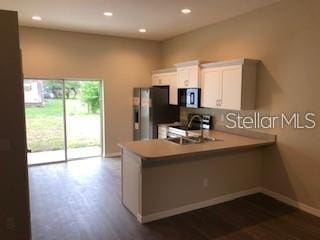 kitchen featuring kitchen peninsula, stainless steel fridge, white cabinets, stove, and sink