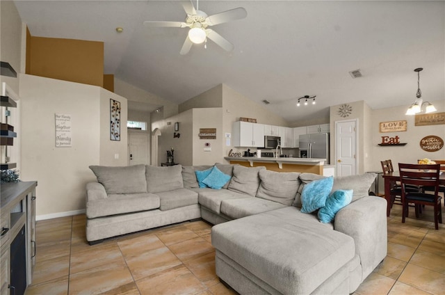 living room with ceiling fan with notable chandelier, rail lighting, light tile patterned floors, and high vaulted ceiling