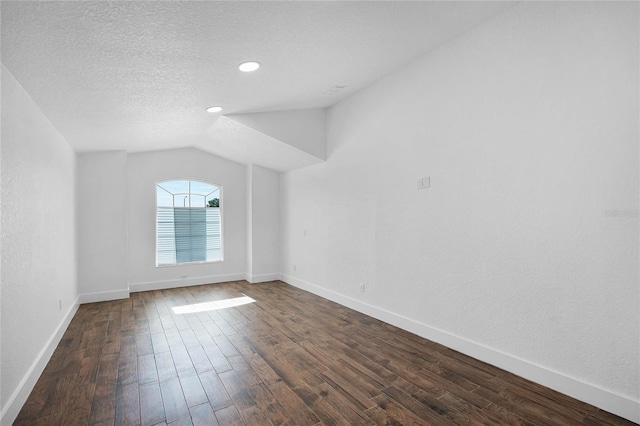 spare room with a textured ceiling, dark hardwood / wood-style flooring, and lofted ceiling