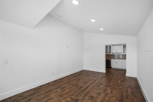 spare room featuring a textured ceiling, dark hardwood / wood-style floors, beverage cooler, and lofted ceiling