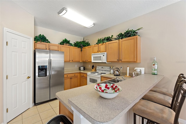 kitchen featuring a kitchen bar, a textured ceiling, light tile patterned floors, kitchen peninsula, and white appliances