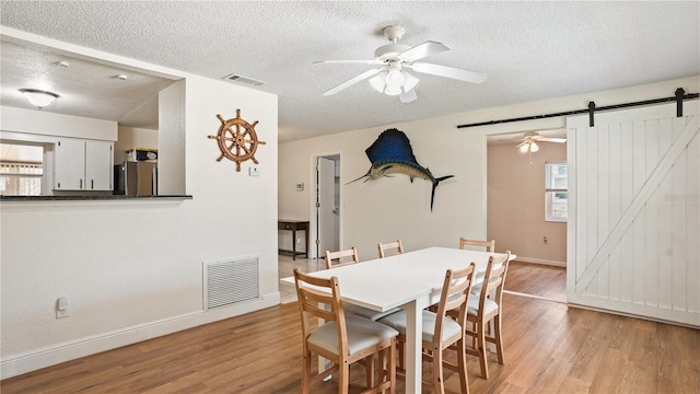 dining area with ceiling fan, a textured ceiling, light hardwood / wood-style flooring, and a barn door