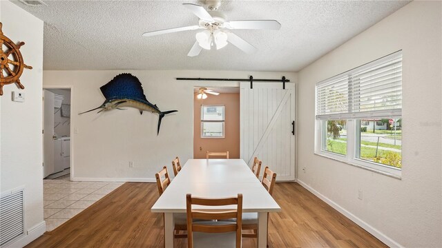 dining space featuring light hardwood / wood-style flooring, a barn door, a textured ceiling, and ceiling fan