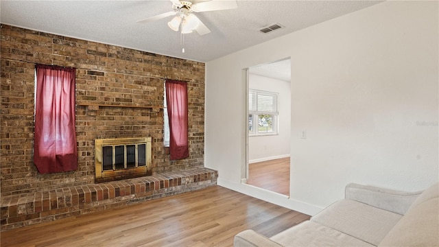 living room with brick wall, a textured ceiling, a brick fireplace, and hardwood / wood-style floors