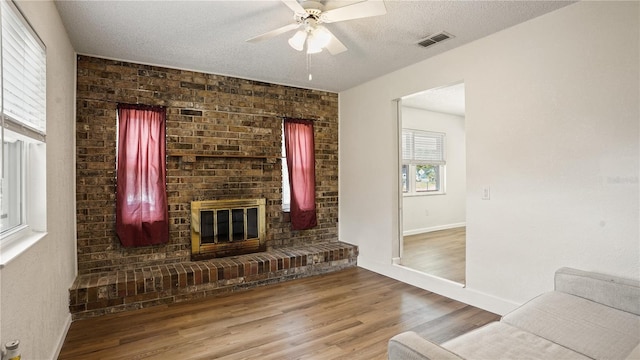 living room featuring a fireplace, wood-type flooring, ceiling fan, brick wall, and a textured ceiling