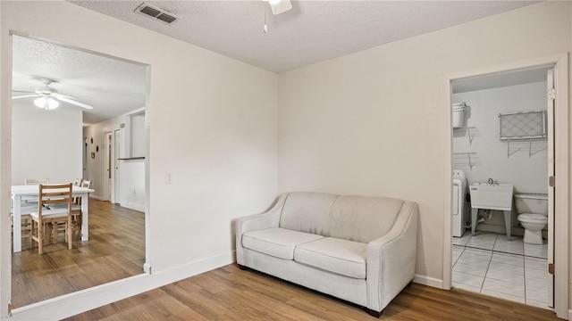 living area with sink, light hardwood / wood-style floors, washer / clothes dryer, a textured ceiling, and ceiling fan