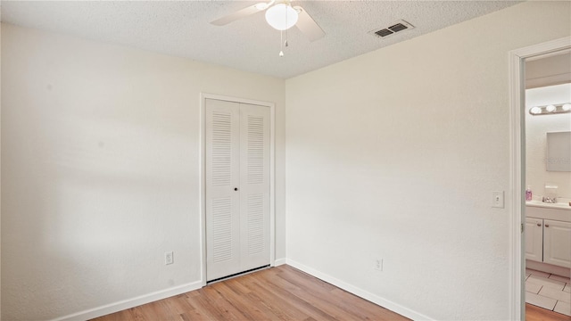 unfurnished bedroom with ensuite bathroom, a closet, light wood-type flooring, a textured ceiling, and ceiling fan