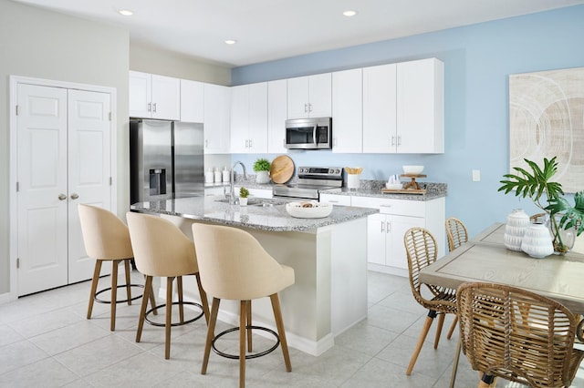 kitchen with white cabinets, light stone countertops, light tile patterned floors, stainless steel appliances, and a kitchen island with sink