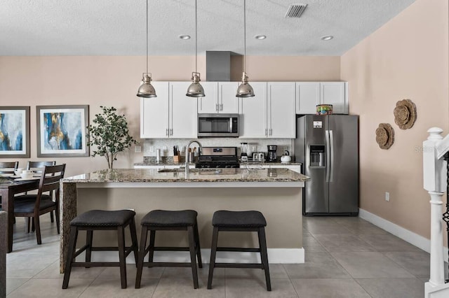 kitchen featuring white cabinetry, hanging light fixtures, appliances with stainless steel finishes, and an island with sink