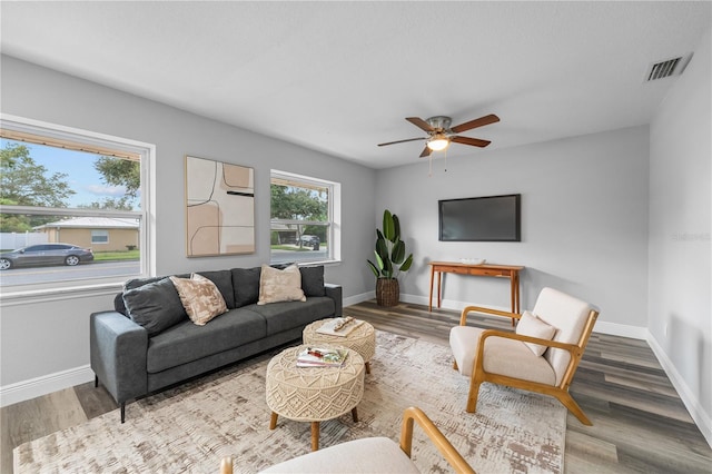 living area with a ceiling fan, wood finished floors, visible vents, and baseboards