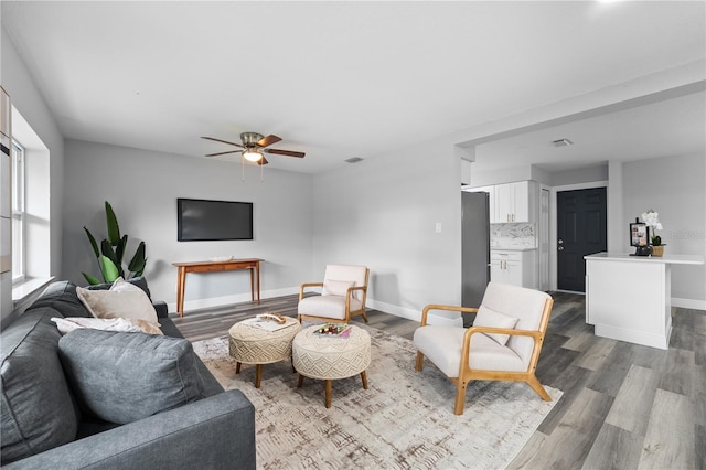 living area with dark wood-style floors, visible vents, a ceiling fan, and baseboards