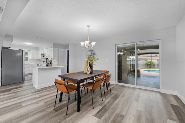 dining area with a textured ceiling, a chandelier, visible vents, baseboards, and light wood-style floors