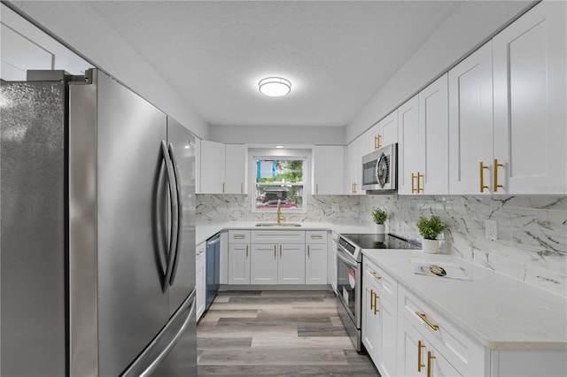 kitchen with a sink, white cabinets, light countertops, appliances with stainless steel finishes, and tasteful backsplash