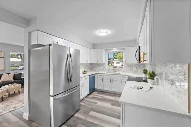 kitchen with tasteful backsplash, appliances with stainless steel finishes, a healthy amount of sunlight, white cabinetry, and a sink