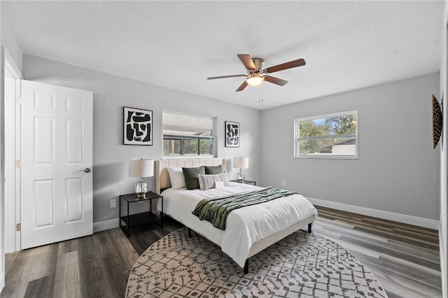 bedroom with a ceiling fan, a textured ceiling, baseboards, and dark wood-type flooring