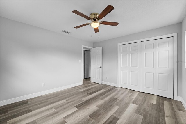 unfurnished bedroom with baseboards, a closet, visible vents, and wood finished floors