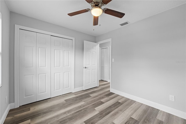 unfurnished bedroom with ceiling fan, wood finished floors, visible vents, baseboards, and a closet