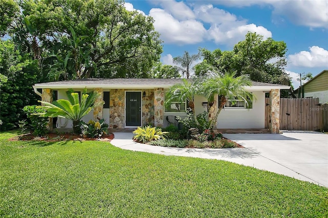 view of front of property featuring stone siding, concrete driveway, fence, and a front lawn