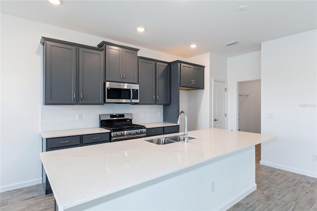 kitchen with light stone countertops, light wood-type flooring, stainless steel appliances, sink, and a center island with sink