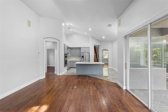 kitchen featuring high vaulted ceiling, stainless steel appliances, wood-type flooring, a center island, and gray cabinetry