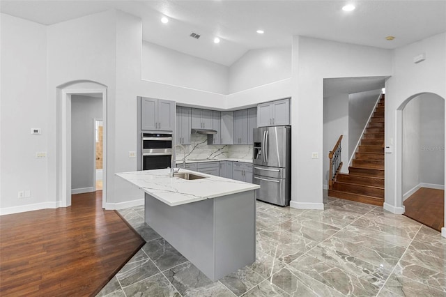 kitchen with a kitchen island with sink, high vaulted ceiling, stainless steel appliances, light stone counters, and sink