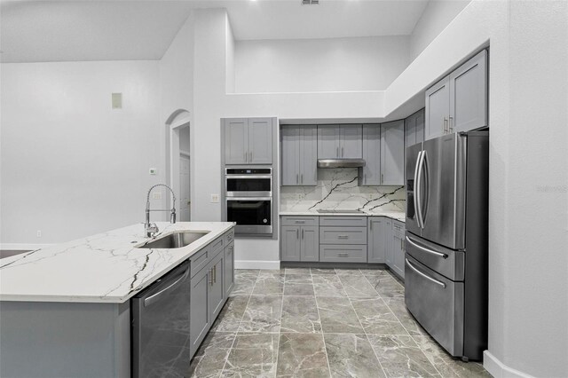 kitchen featuring gray cabinetry, appliances with stainless steel finishes, light stone counters, sink, and decorative backsplash