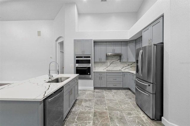 kitchen featuring sink, tasteful backsplash, light stone counters, appliances with stainless steel finishes, and gray cabinets