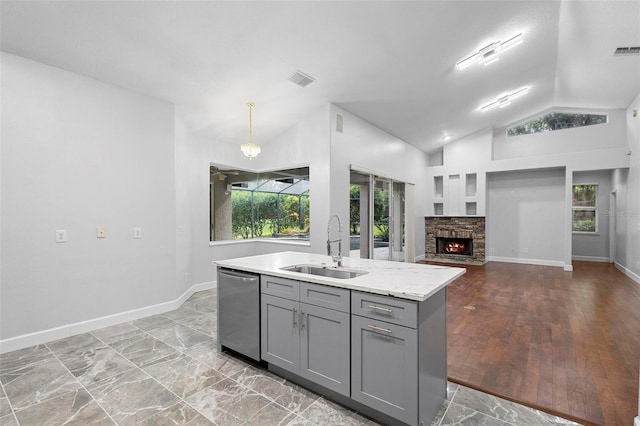 kitchen with hanging light fixtures, dishwasher, light wood-type flooring, sink, and a stone fireplace