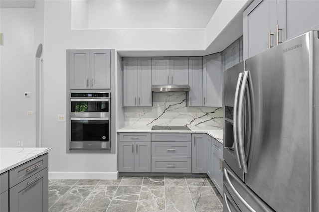 kitchen featuring backsplash, light stone counters, stainless steel appliances, and gray cabinetry