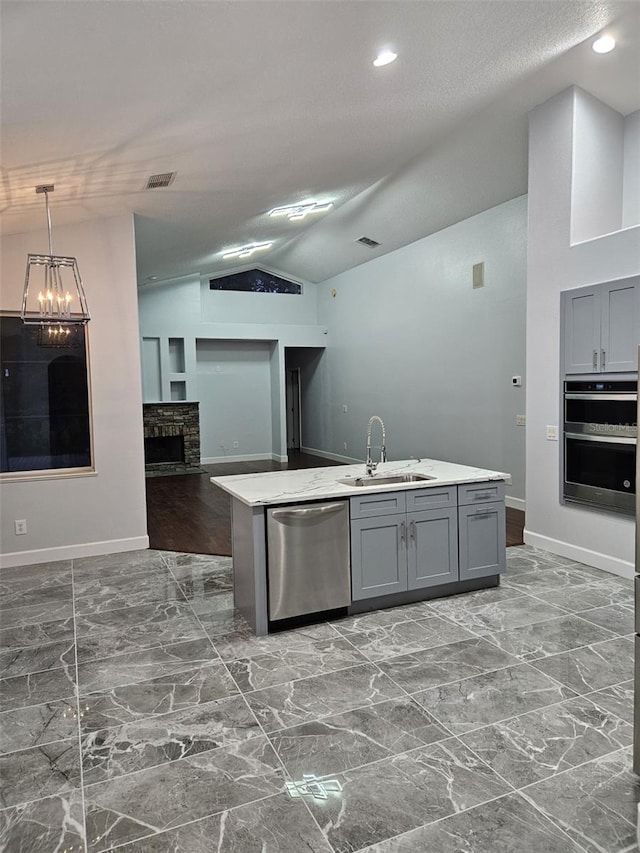 kitchen featuring a chandelier, stainless steel appliances, sink, a stone fireplace, and lofted ceiling