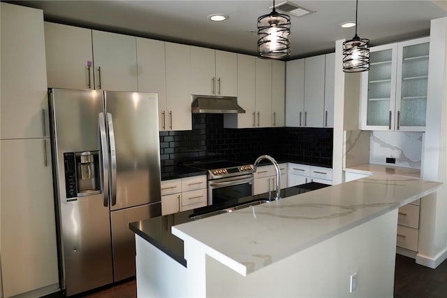 kitchen with decorative backsplash, appliances with stainless steel finishes, hanging light fixtures, and a center island with sink