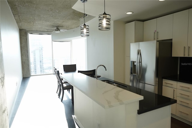 kitchen with sink, decorative light fixtures, stainless steel fridge, a wall of windows, and a kitchen island with sink