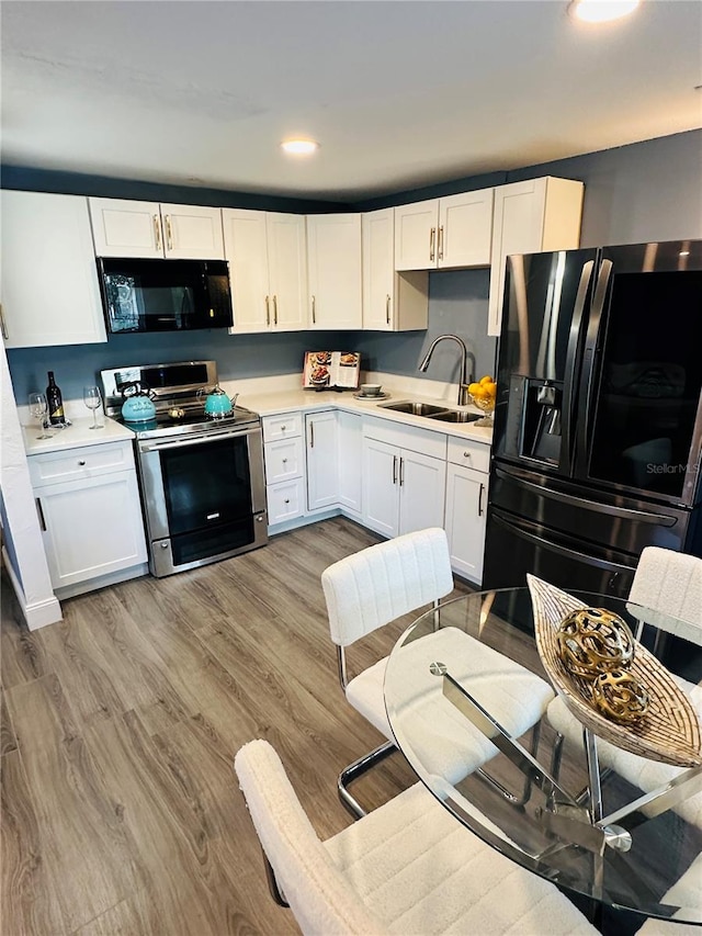 kitchen with white cabinetry, sink, light hardwood / wood-style flooring, and black appliances