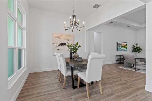 dining space with a tray ceiling, a chandelier, and light hardwood / wood-style flooring