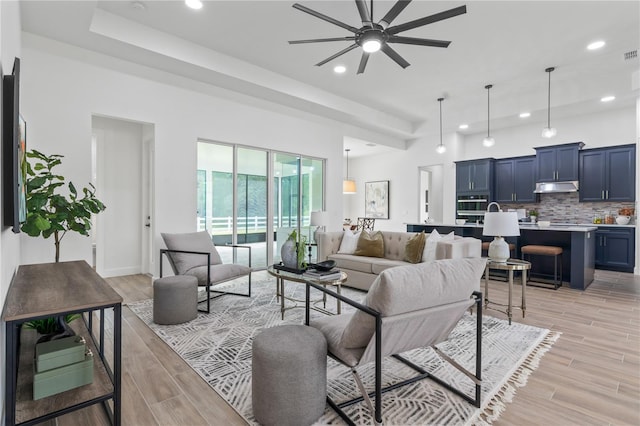 living room featuring a tray ceiling, light hardwood / wood-style floors, and ceiling fan