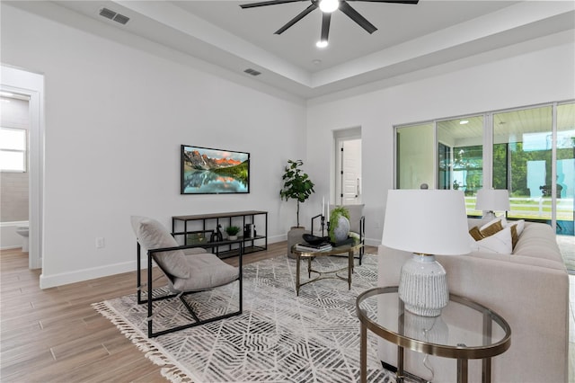 living room featuring a tray ceiling, light hardwood / wood-style flooring, and ceiling fan