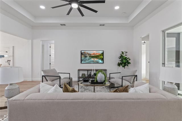 living room featuring a tray ceiling, light hardwood / wood-style flooring, and ceiling fan