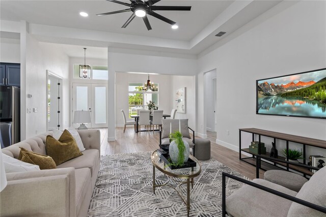 living room featuring ceiling fan with notable chandelier and light wood-type flooring