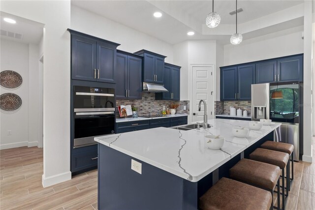 kitchen featuring stainless steel appliances, a center island with sink, sink, a kitchen breakfast bar, and blue cabinetry